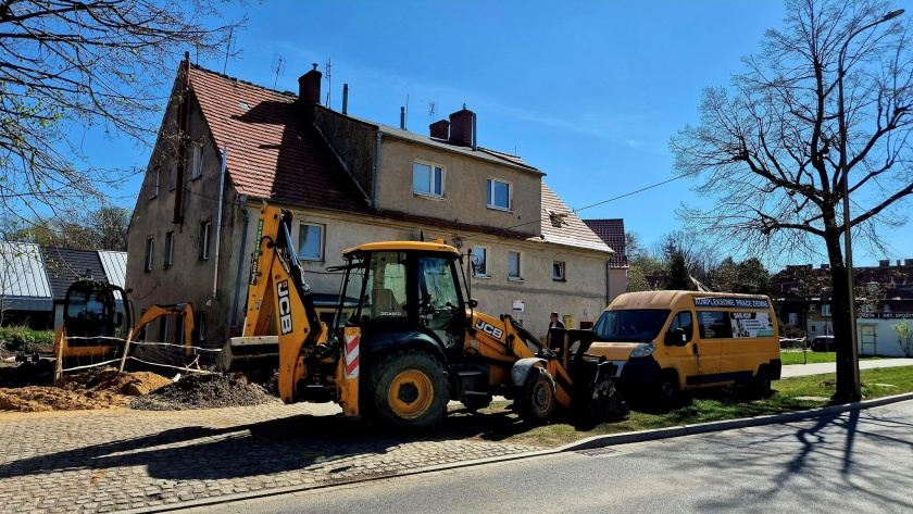 Termomodernizacja gminnego budynku wielorodzinnego. Przed budynkiem specjalistyczne pojazdy